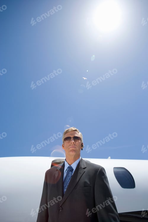 Preview: Vertical Shot Of A Businessman In Sunglasses By Airplane With A Sun Flare In The Background.