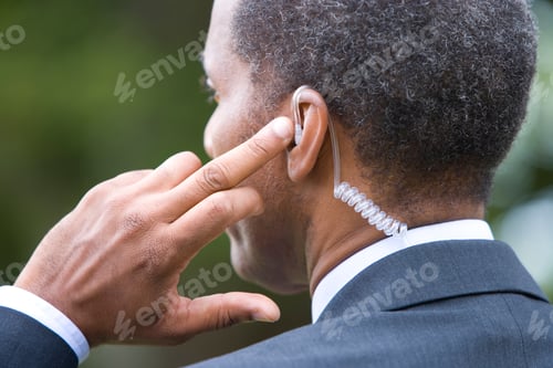 Preview: Rear View Of A Senior Businessman In A Formal Business Suit Wearing An Earpiece And Holding Up A