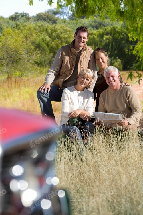 Preview: Vertical Portrait Of Two Generations Of Family Sitting With A Map By The Roadside In Front Of A Car