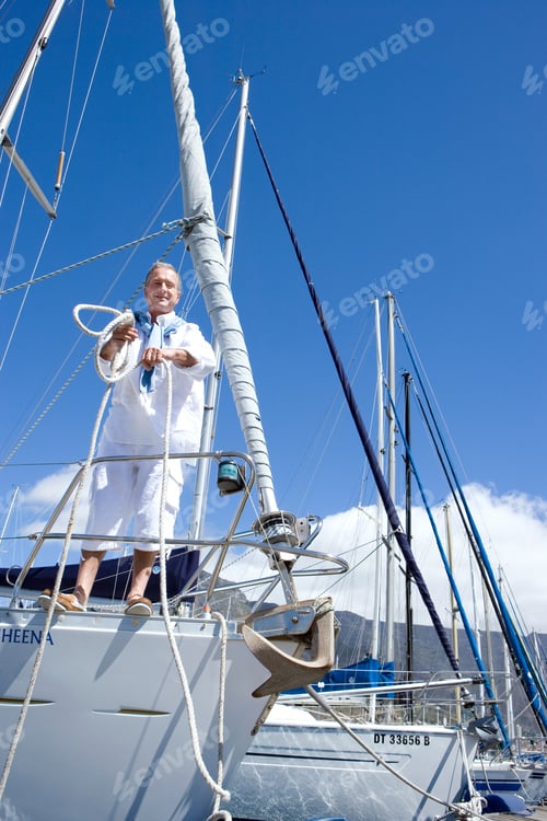 Preview: Senior Man Standing On The Deck Of His Yacht In The Harbor While Holding A Mooring Rope And Smiling
