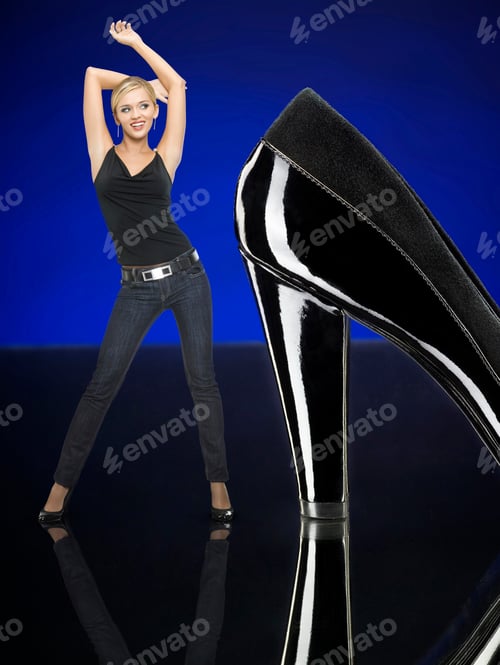 Preview: Woman Is Standing Next To Black, High-Heeled Shoe With Her Arms Up In The Air.