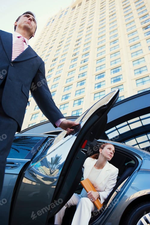 Preview: Vertical Low Angle Shot Of A Chauffeur Opening The Car Door For A Businesswoman Outside The Office