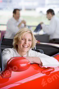 Preview: Vertical Shot Of A Woman Sitting In A Red Convertible Smiles At The Camera With A Salesman Showing