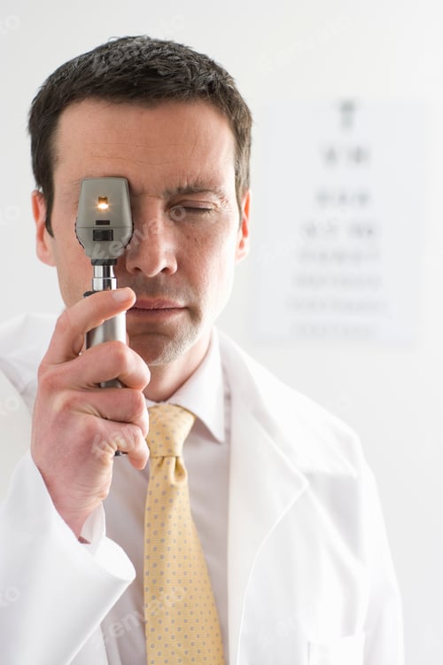 Preview: A Doctor In Sharp Focus Looking Through An Ophthalmoscope With An Eye Chart In The Background