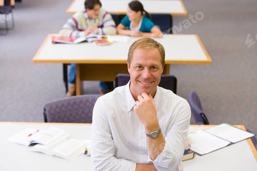 Preview: A Mature Man Standing In The Library With One Hand On His Chin By Students Studying In The