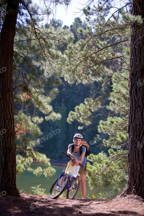 Preview: Vertical Shot Of A Young Woman Leaning On A Mountain Bike Along A Woodland Trail Beside A Lake