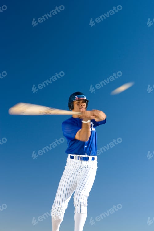 Preview: Vertical Low Angle Front View Of A Baseball Batter Standing Against Clear Blue-Sky Hitting The Ball