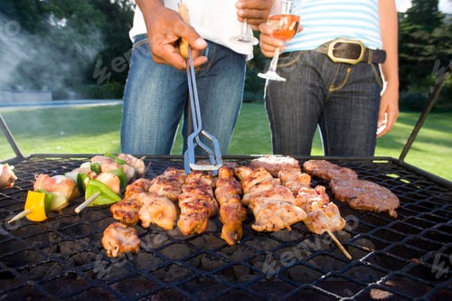 Preview: Horizontal Mid Section Of A Couple Having Barbeque Outdoors Stand By The Grill With Wine Glasses In