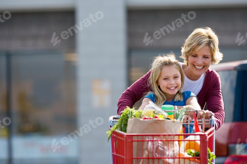 Preview: Waist Up Shot Of A Joyous Mother And Daughter Pushing A Shopping Trolley In A Supermarket Car Park