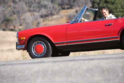 Preview: Tilted Low Angle Profile Shot Of A Woman Driving A Red Convertible On A Sunny Day Smiling At The