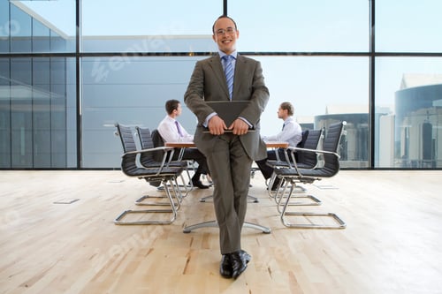 Preview: Confident Businessman Holding His Laptop In A Conference Room And Smiling At The Camera With Two Of