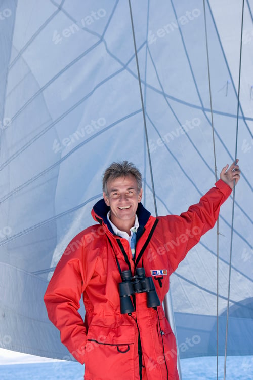 Preview: Front View Of A Man In Red Jacket With Binoculars Hanging Around Neck Standing Below Sail On The