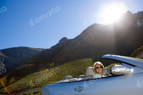 Preview: Side View Portrait Of A Smiling Senior Woman Driving A Convertible Silver Car Along The Mountain