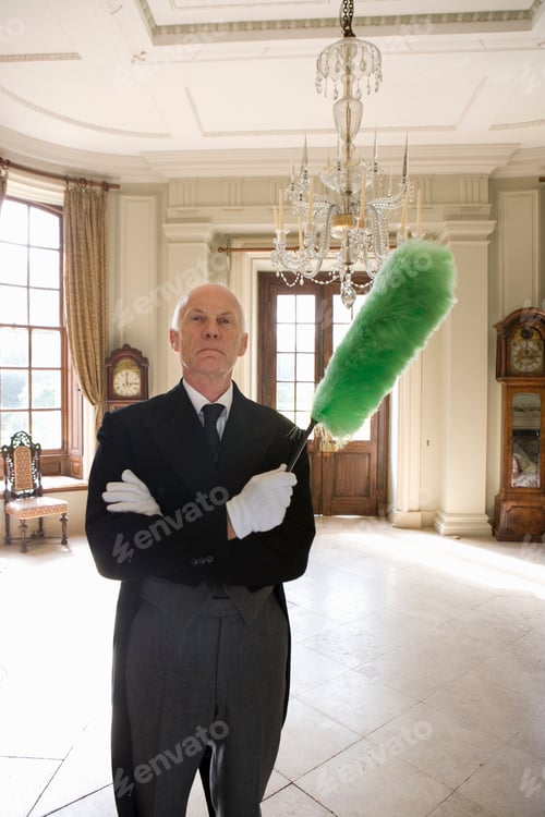 Preview: Vertical Shot Of A Butler Standing With Arms Crossed And Holding A Duster In His Hands While