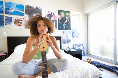 Preview: Horizontal Portrait Of A Teenage Girl Sitting On Bed With Hands On The Electric Guitar Looks At The