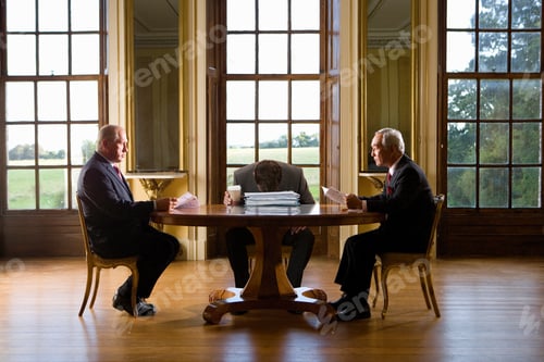 Preview: Horizontal Profile Shot Of Two Senior Businessmen Sitting Across A Table With A Third Man In Middle