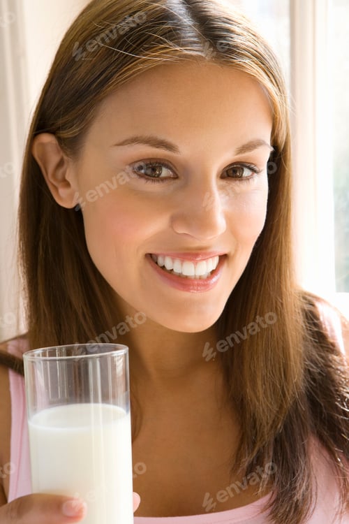Preview: Vertical Head And Shoulder Portrait Of A Young Woman With A Glass Of Milk Smiles At The Camera.