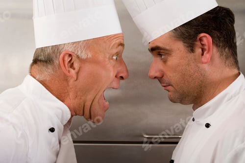 Preview: Close-Up Portrait Of An Angry Senior Chef Yelling At The Junior Chef In A Commercial Kitchen.