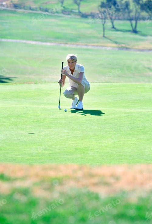Preview: Vertical Shot Of A Mature Woman Crouching On The Golf Course On A Sunny Day.
