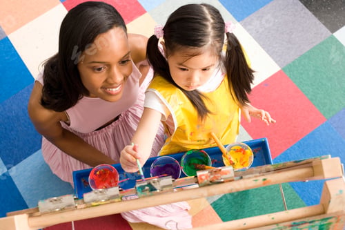 Preview: Close Up Of Top View Of A Young Teacher Kneeling Down And Smiling Next To A Little Girl Who Is