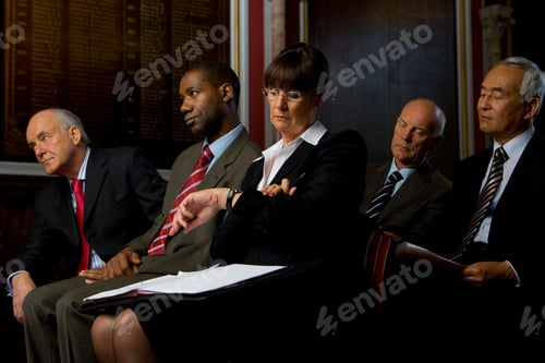 Preview: Businesswoman Sitting In The Hall With Paperwork Looking At Watch By Wall Plaque In Background.