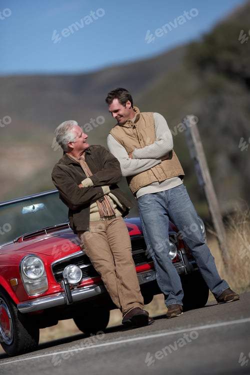 Preview: Vertical Tilted Full Length Shot Of A Senior Man With His Son Standing Besides A Red Convertible