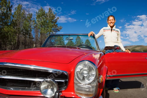 Preview: Horizontal Low Angle Shot Of A Young Woman Standing Besides The Door Of Her Red Convertible Smiles