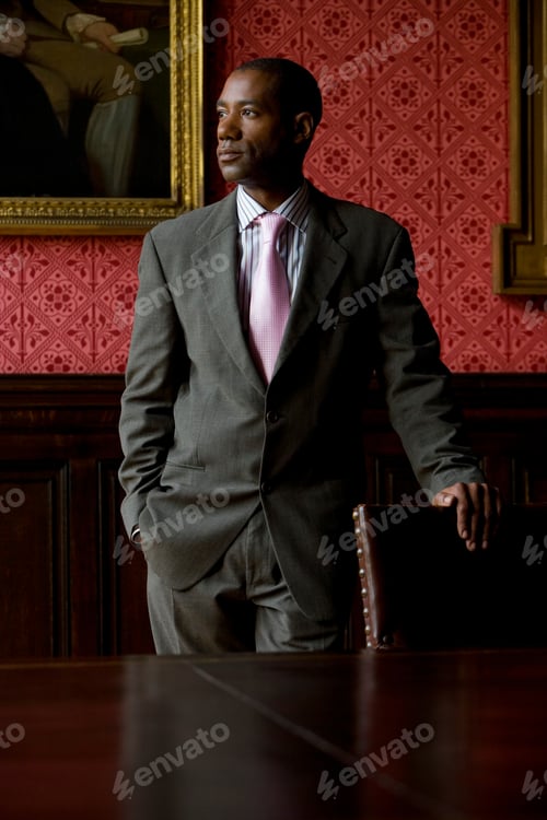 Preview: Portrait Of A Young Businessman Standing Behind The Table With A Hand On A Chair Looking Away From