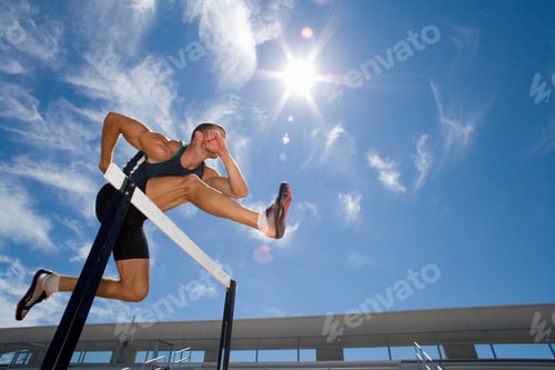 Preview: Low Angle View Of A Male Athlete Jumping Over The Hurdle With The Background Of Sun Flare And Blue
