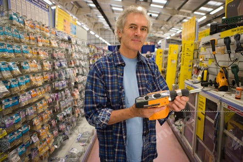Preview: Waist Up Portrait Of A Man Holding A Power Tool In Hand Smiles At The Camera While Shopping In An