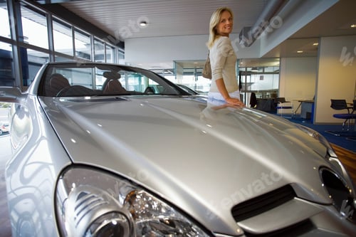 Preview: Portrait Of An Attractive Woman Leaning Against A New Silver Convertible Car In The Large Showroom.