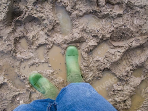 Preview: Top View Of A Person In Rubber Boots Standing In Puddles Of Muddy Water With Copy Space.