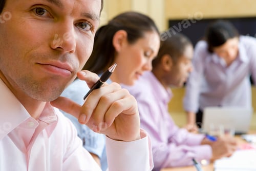 Preview: Young Businessman With His Hand On His Chin Looking Down And Frowning While His Colleagues Are