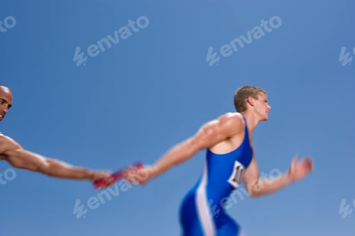 Preview: Young Male Athlete Receiving A Relay Baton From His Teammate On A Bright, Sunny Day At An Athletics