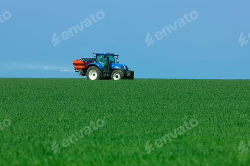Preview: A Blue Colored Tractor Spreading Fertilizer On A Bright Sunny Day In A Lush Green Field With A