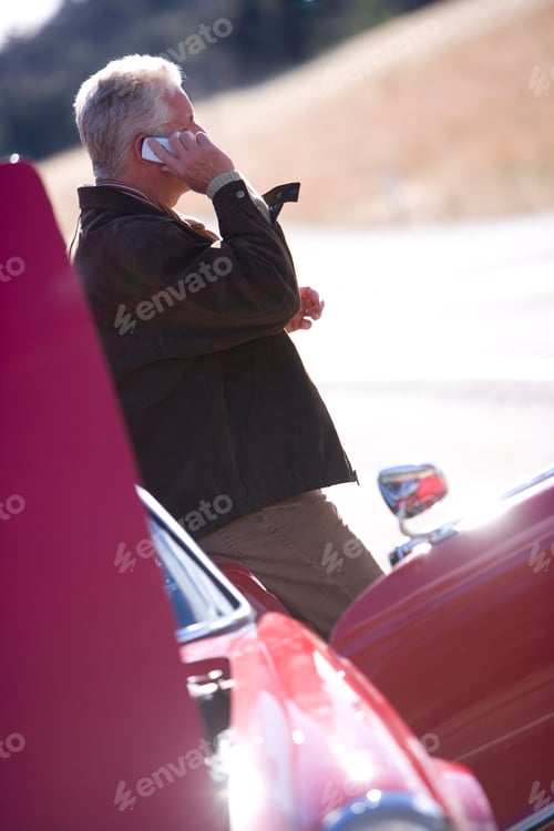 Preview: Vertical Tilted Shot Of A Senior Man Calling For Help On A Cell Phone Leaning On A Broken Down Red