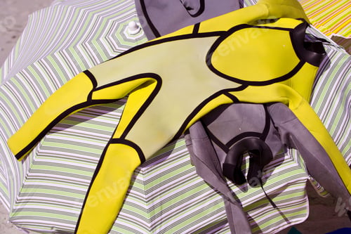 Preview: Couple Of Wetsuits Placed On Top Of An Umbrella At The Beach On A Bright, Sunny Day