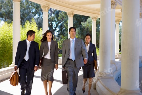 Preview: Horizontal Shot Of Four Business Colleagues Walking Side By Side In A Colonnade On A Sunny Day.