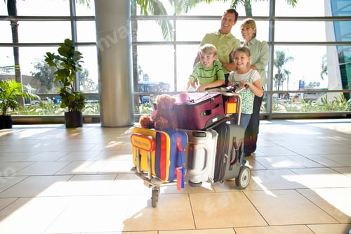 Preview: A Happy Family Standing With Luggage Trolley In An Airport Lounge Looking Sideways.
