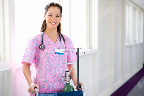 Vista previa: Young Female Nurse Standing In The Hospital Corridor With And Empty Wheelchair And Smiling At The