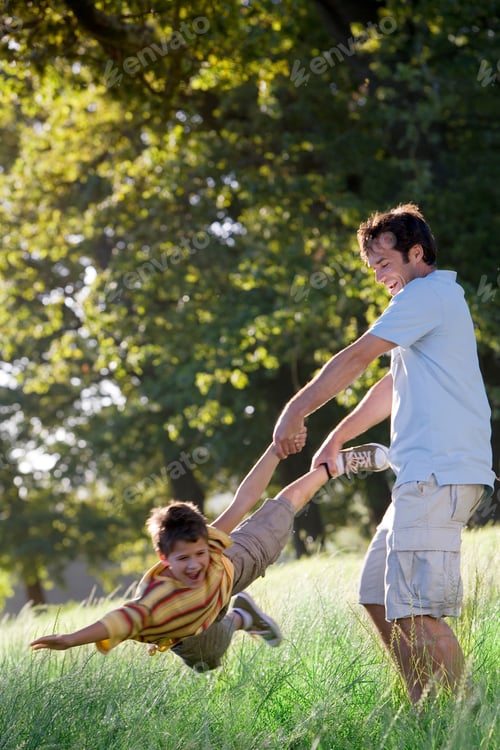 Preview: Vertical Shot Of A Father Swinging Son In A Woodland Clearing As He Screams On A Sunny Day.