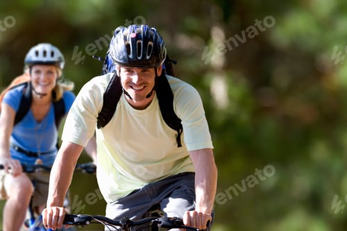 Preview: Young Man Riding A Bicycle In A Park With A Smile On Face Looking At Camera And Female Rider In