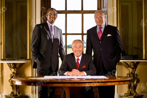 Preview: Senior Businessman Sitting At His Desk In His Office Surrounded By Two Of His Colleagues Who Are
