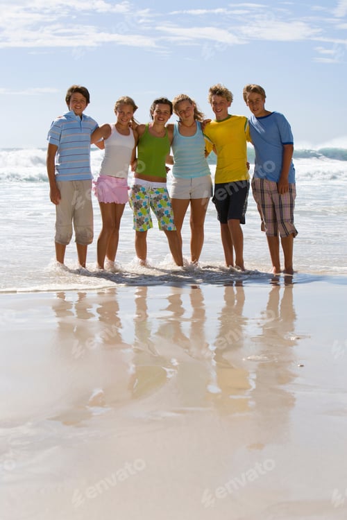 Preview: Group Of Teenagers Standing Arm In Arm On The Beach On A Bright, Sunny Day And Smiling At The Camera