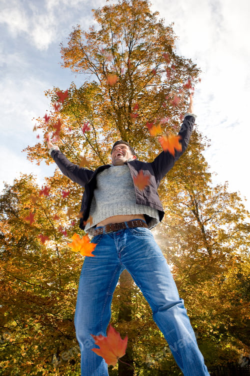 Preview: Man Jumping And Throwing Many Fallen Leaves Up In The Air In The Autumn Fall Season With Yellow