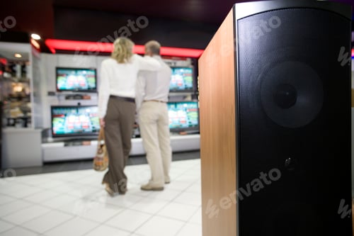 Preview: Selective Focus On Speaker In Foreground With A Senior Couple Admiring Tv Sets In The Background In