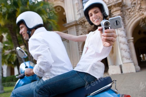 Preview: Portrait Of A Young Couple Riding On A Blue Motor Scooter And Woman Filming With A Portable Video