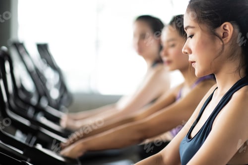 Preview: Side View Of Young Women Sitting On Exercise Bikes In Gym