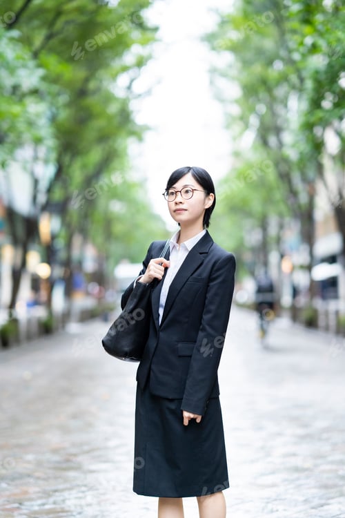 Preview: A Young Woman In A Suit Standing On A Street Lined With Roadside Trees