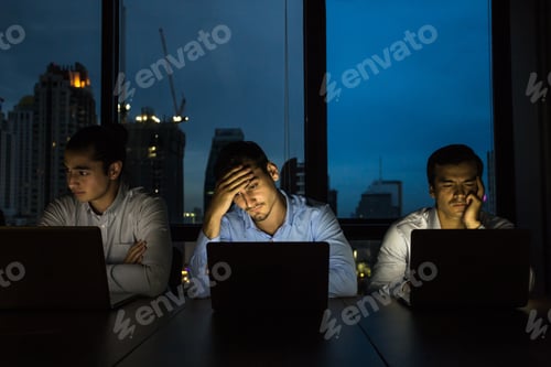 Preview: Business Team Working Late At Night With Lights Off And Computers Laptop Screen Light On. Business